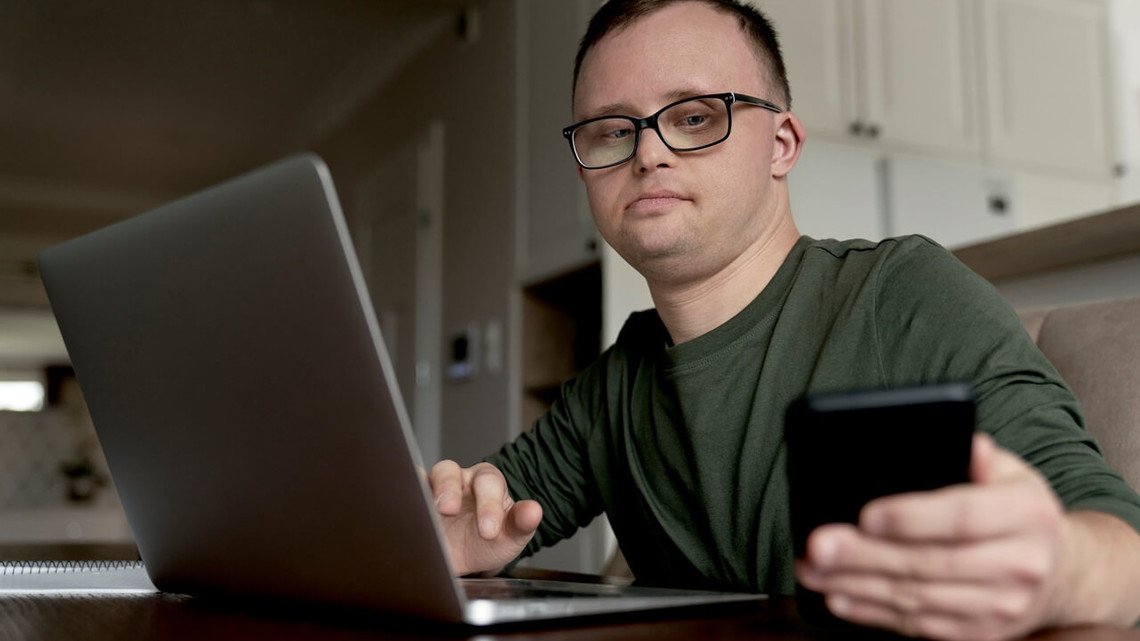 Mann mit Down Syndrom bedient Laptop und Smartphone
