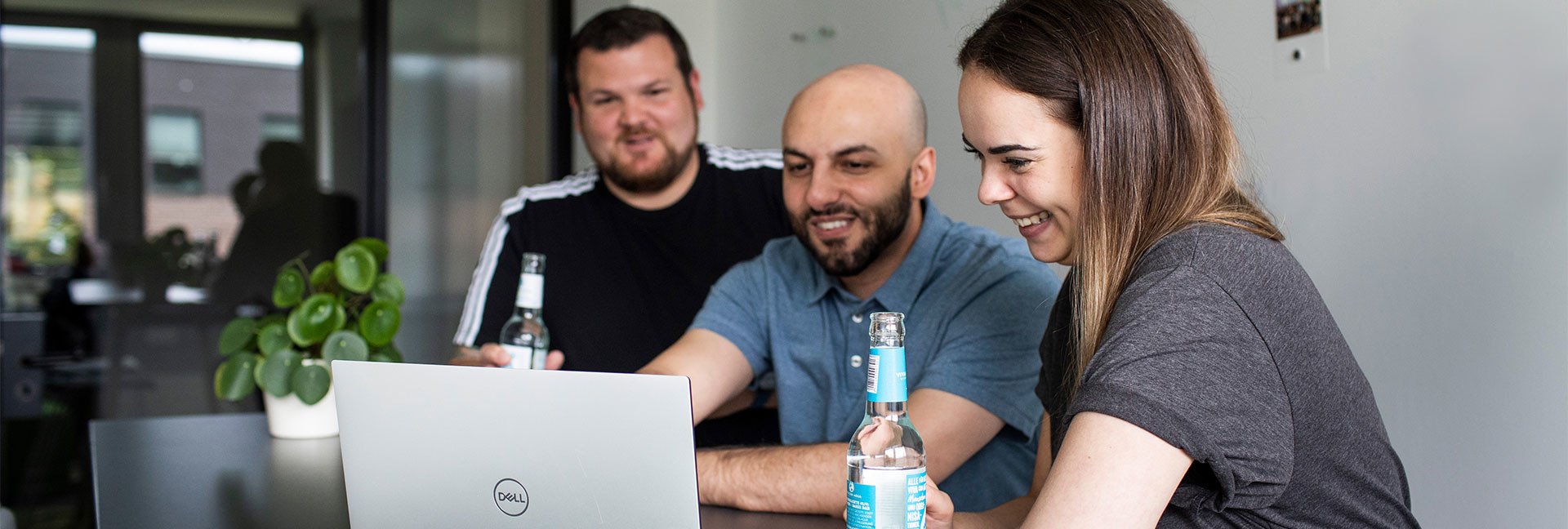 Drei Personen schauen gemeinsam lächelnd auf einen Laptop