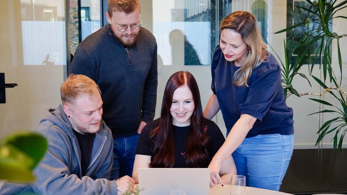 Zwei junge Frauen und Männer sitzen vor einem Laptop am Tisch