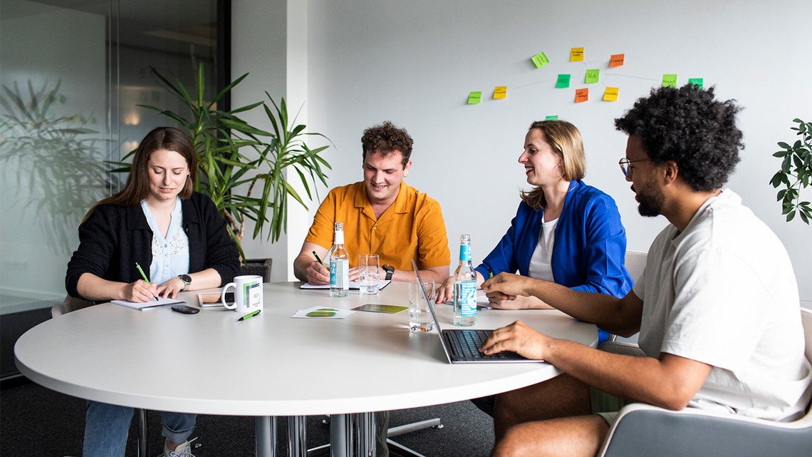 Digitalagentur: Personen sitzen im Meeting im Konferenz-Raum und halten Notizen fest.