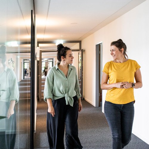 mindshape-Agenturleben: Mitarbeiter:innen schlendern zu zweit über den Flur im Büro.