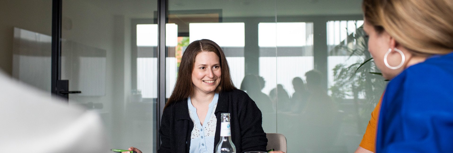 Junior Performance Marketing Manager SEA/PPC (m/w/d) Junior Performance Marketing Manager SEA/PPC (m/w/d): Mehrere Personen sitzen während eines Meetings an einem Tisch.